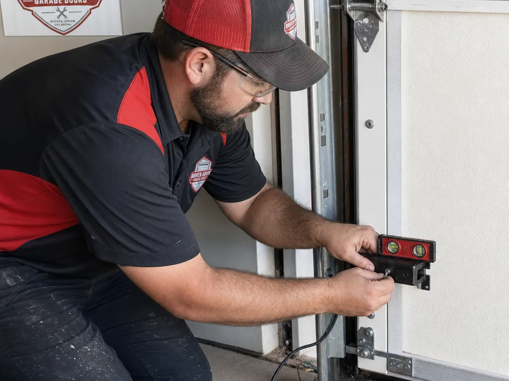 Contractor aligning garage door safety sensors near the bottom of the door track with a level